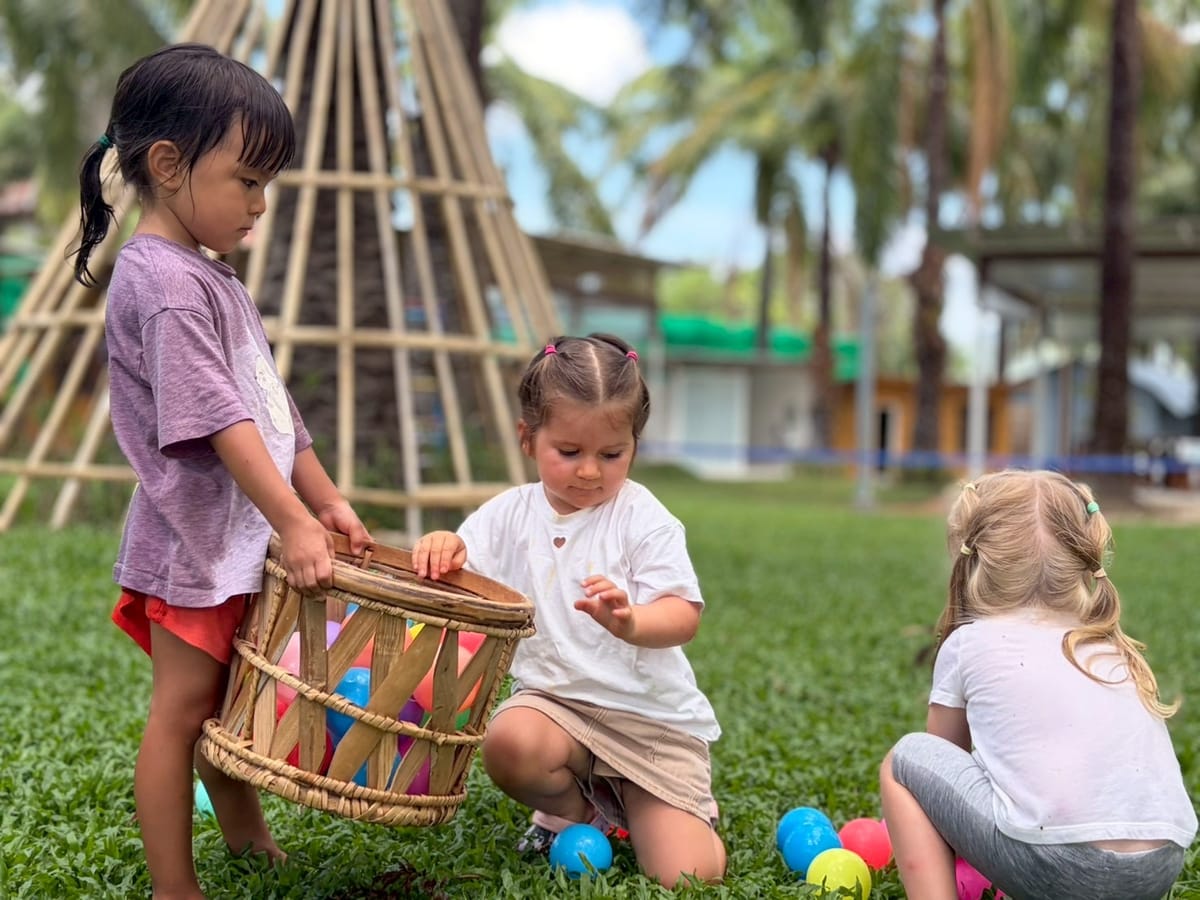 Young children collecting coloured eggs in a basket on the grass