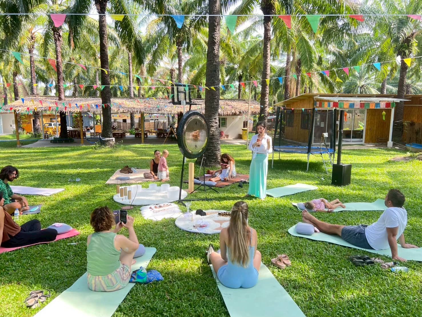 Families on mats on the grass at a sound healing session under the palm trees