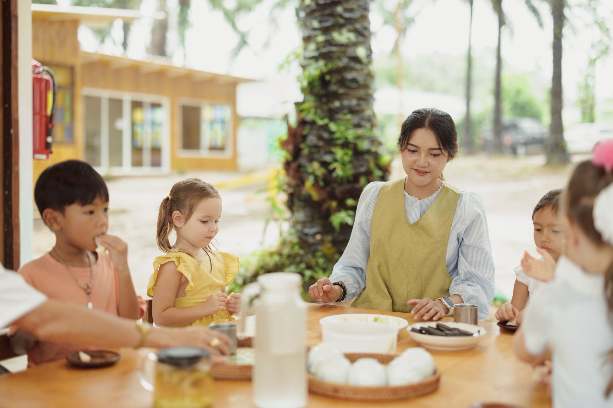 Children and teacher eating together under palm trees at Bamboo Valley